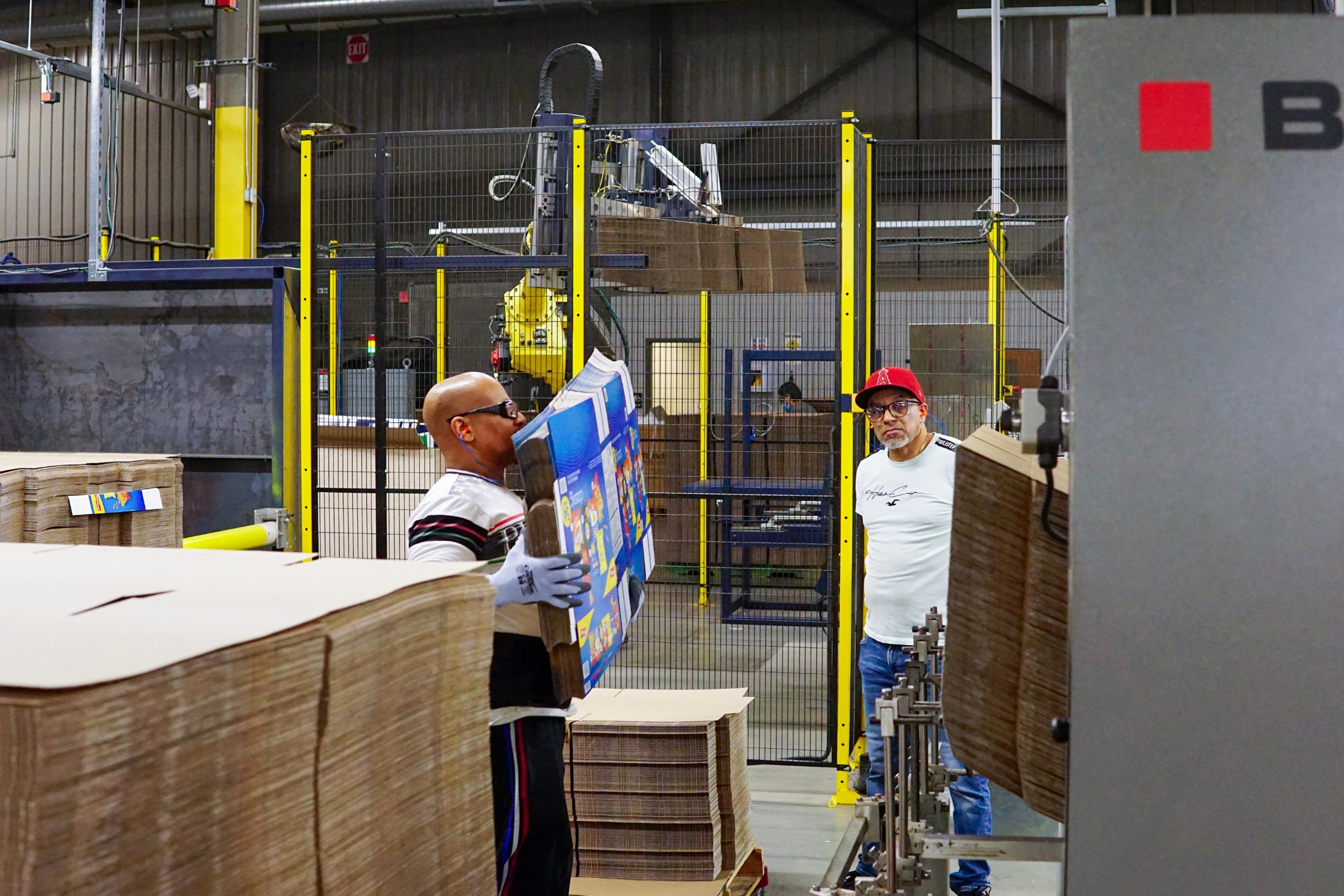 2 men loading a machine vs. a robot.